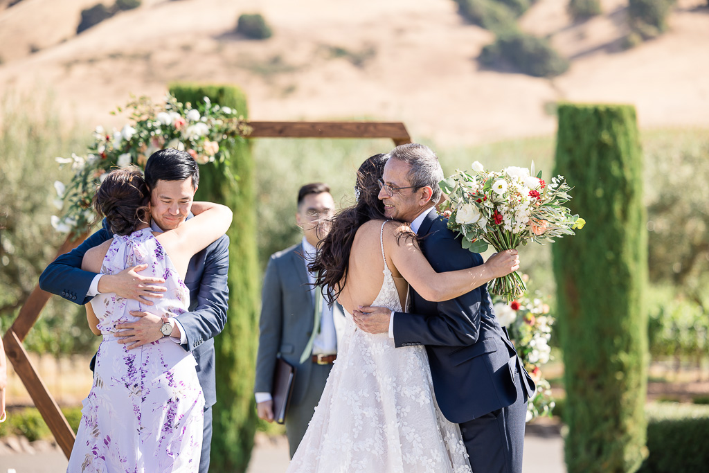 groom giving bride's parents hugs as they bring her to him