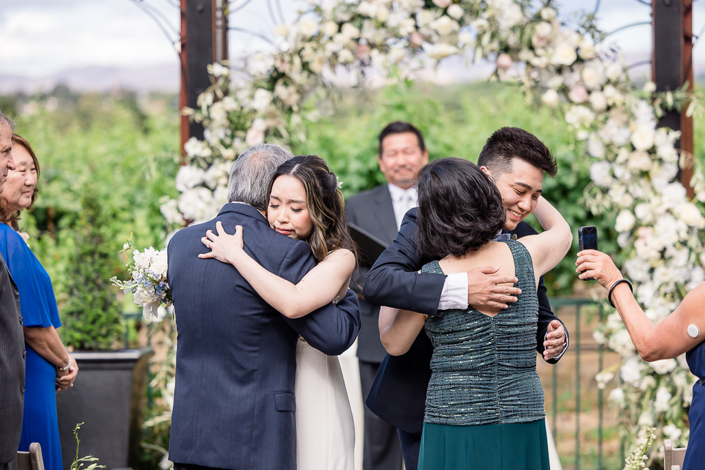 bride and groom hugging parents simultaneously