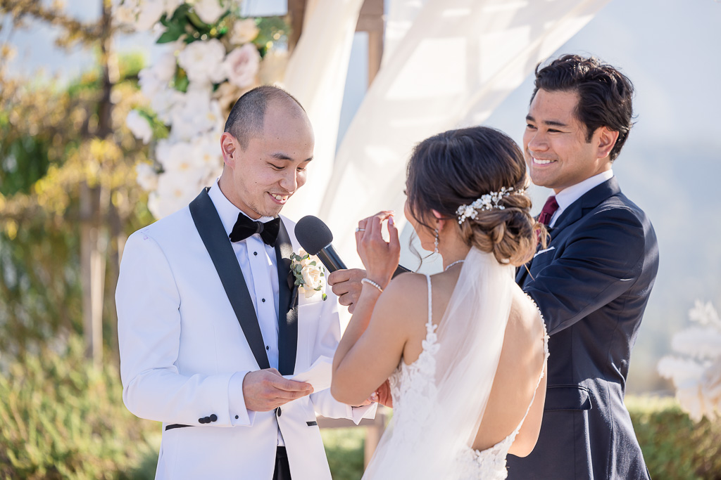groom wearing white tux reading wedding vows