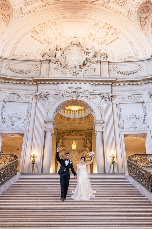 bride and groom cheering as they walk down long staircase