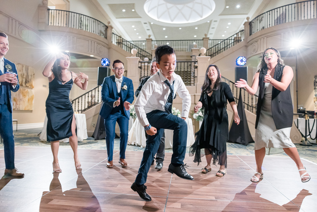 young boy in a suit and tie dancing energetically in the middle of the dance floor