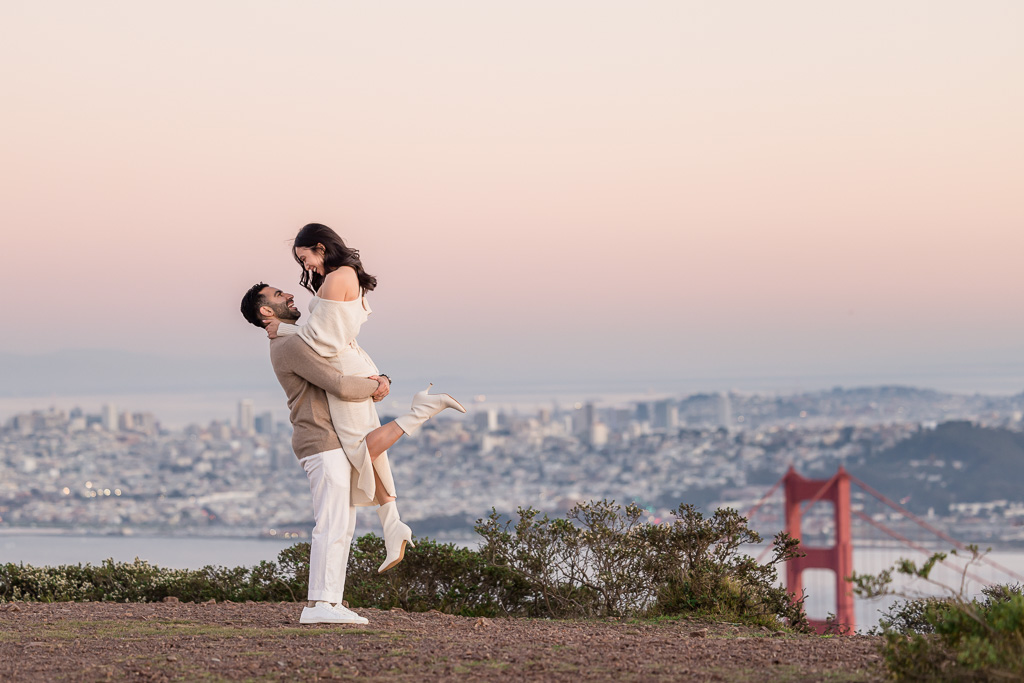 lifting up engagement photo above the San Francisco skyline over the Bay