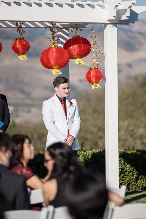 groom standing under wedding arbor with red lanterns