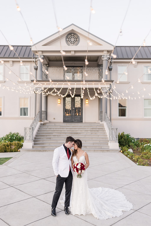 groom in white jacket with his bride in front of white colored mansion