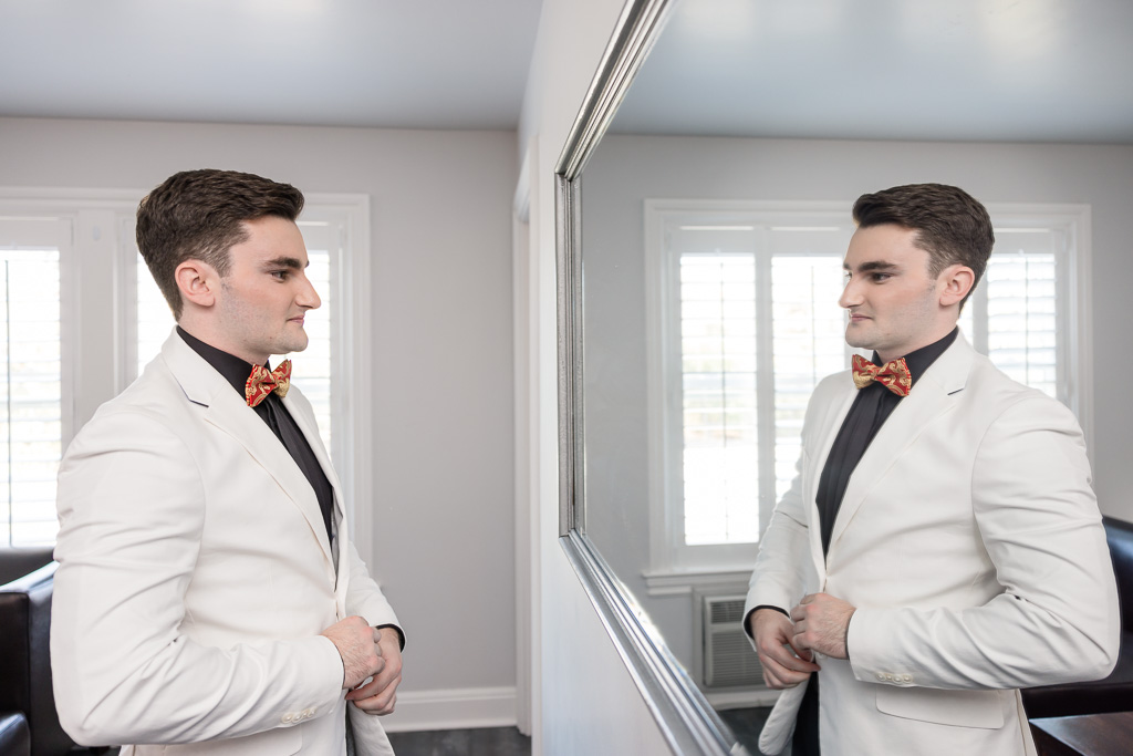 groom buttoning up jacket in front of mirror