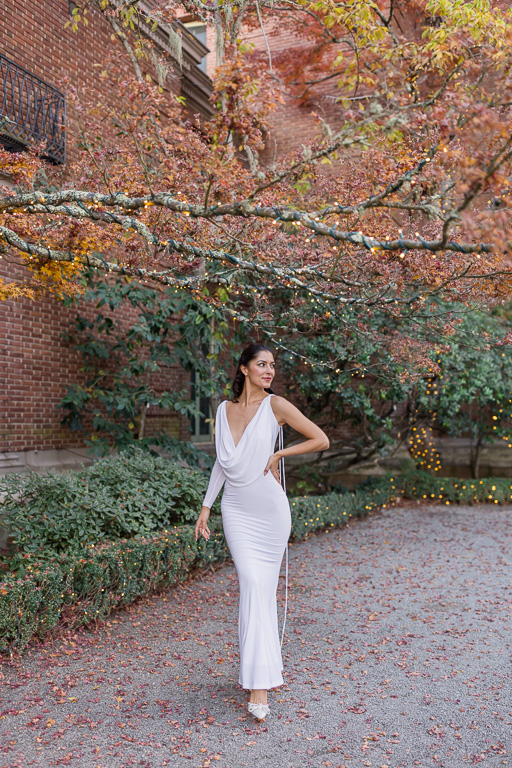 portrait of woman in whithe dress in front of fall foliage against of brick wall