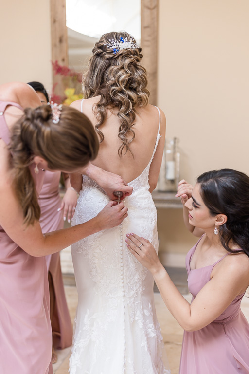 bridesmaids helping bride button up her dress