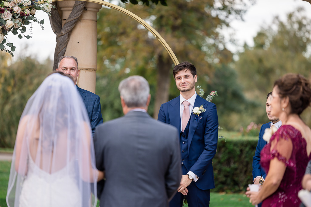emotional photo of groom watching bride and dad walk down the aisle towards him