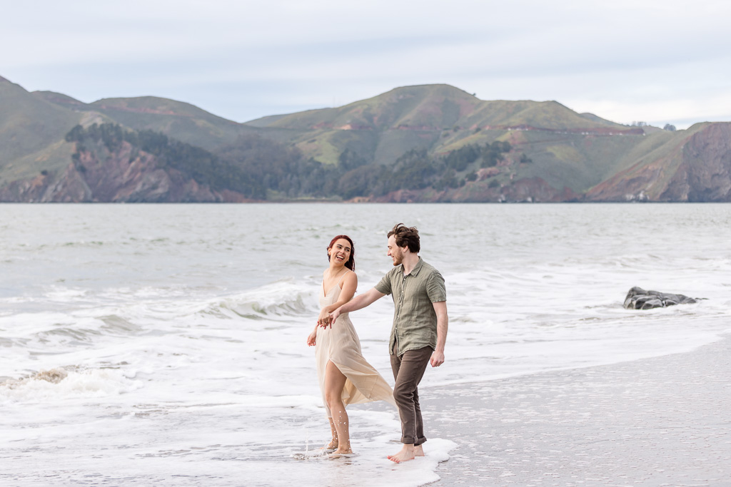 couple playing in the Pacific Ocean for the engagement photos