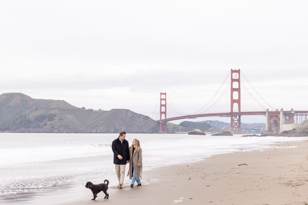 couple walking with dog on a beach in front of the Golden Gate Bridge
