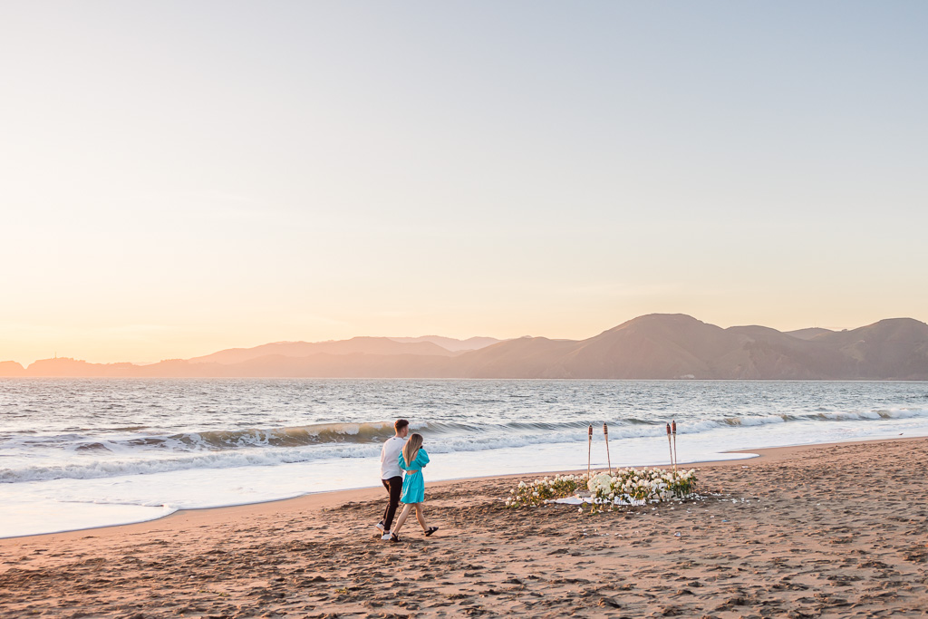 couple walking towards proposal decor on the beach at sunset