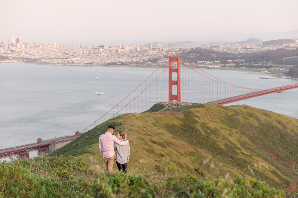 couple standing on hill looking towards Golden Gate Bridge