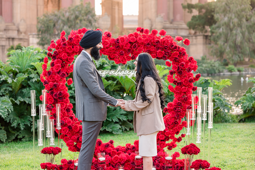 couple standing in front of giant heart made of roses about to propose