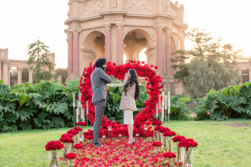 golden hour surprise proposal in front of heart shaped rose arch