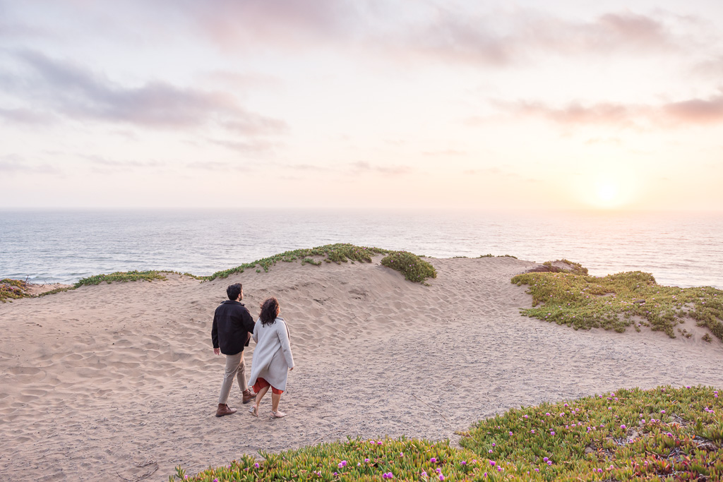couple walking along sand dunes towards ocean cliffs
