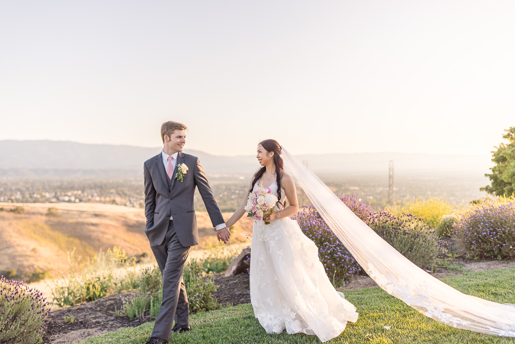 bride wearing a long veil walking with groom at sunset