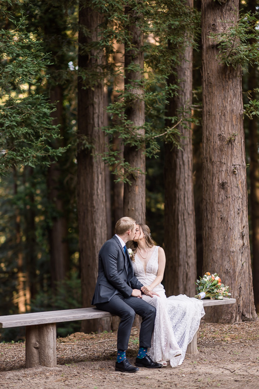 wedding photo of bride and groom sitting on a wooden bench in the woods