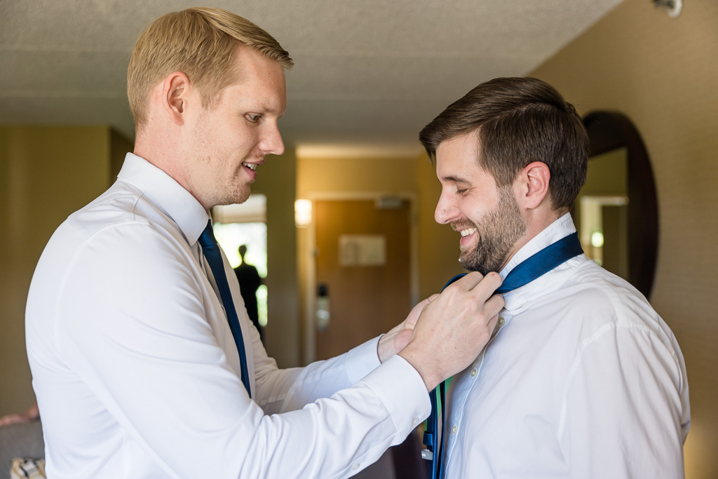 groom helping groomsman with a tie