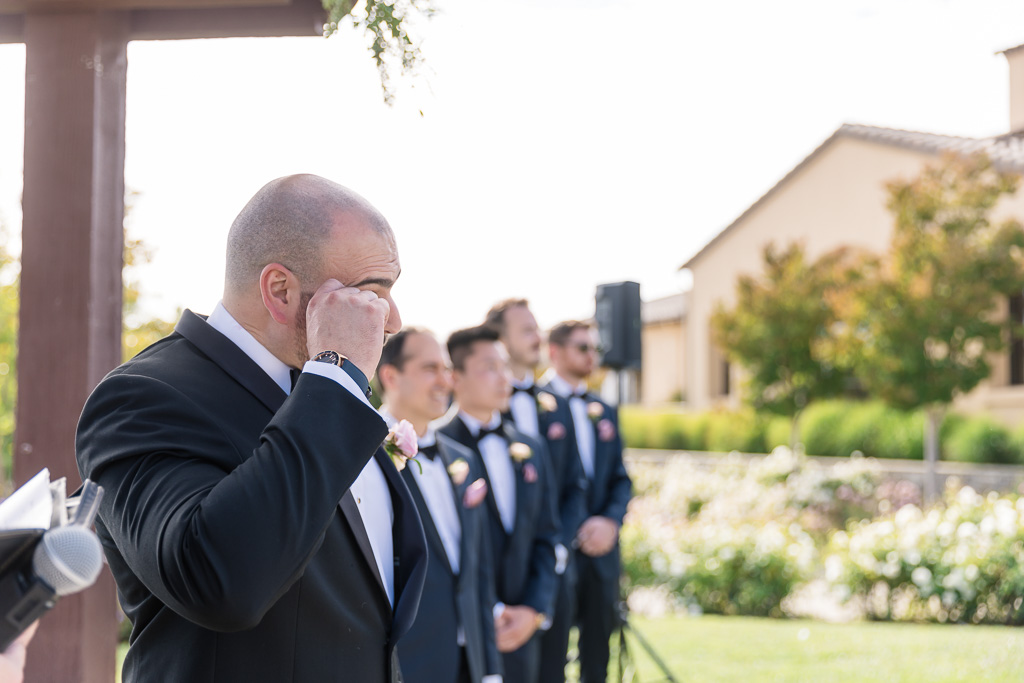 groom wiping a tear as he watches his bride approach