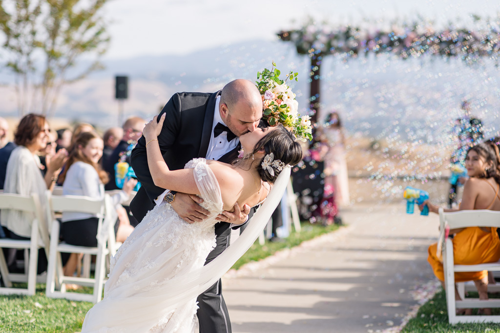 dip and kiss at the end of the aisle with bubbles behind them