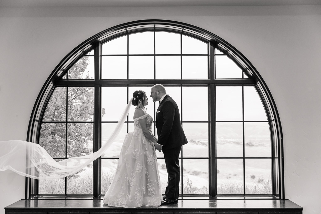 dramatic black & white portrait of bride and groom standing in front a large arch window