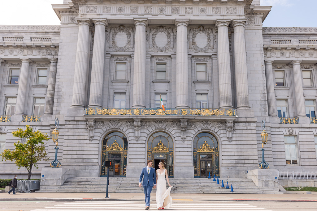 bride and groom crossing the street at the crosswalk in front of SF City Hall