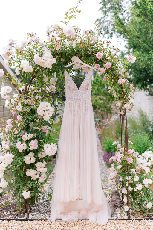 blush tulle wedding dress hanging on floral arch