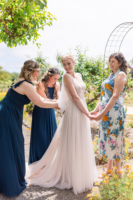 mom and bridesmaids helping bride with her dress and laughing candidly
