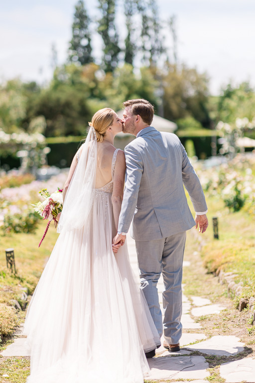 candid photo of bride and groom walking and giving each other a kiss in a garden
