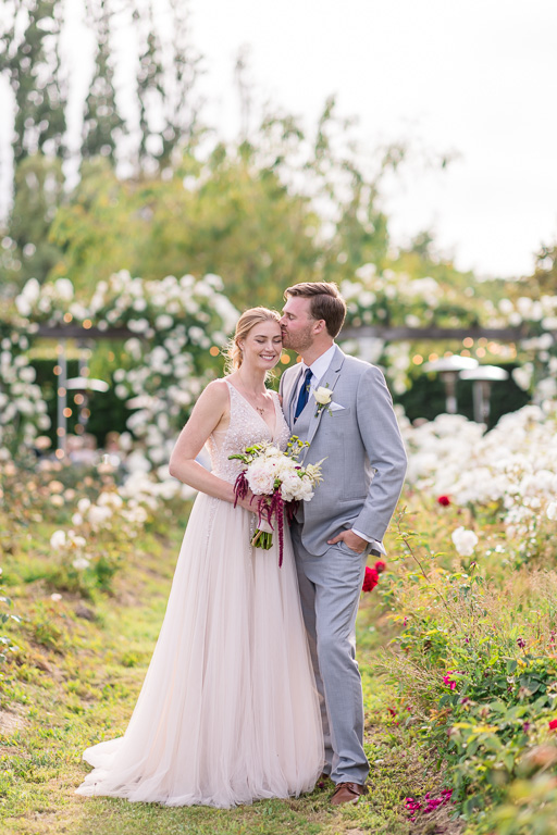 groom giving the bride a kiss under soft sunlight in a rose garden