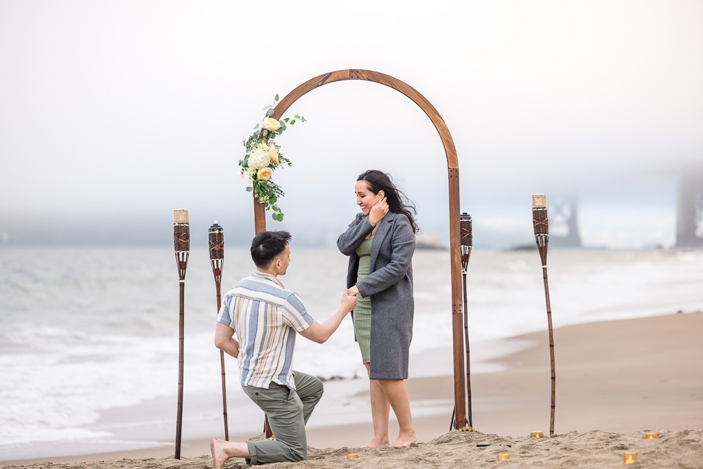 surprise proposal in front of DIY proposal decor on the beach
