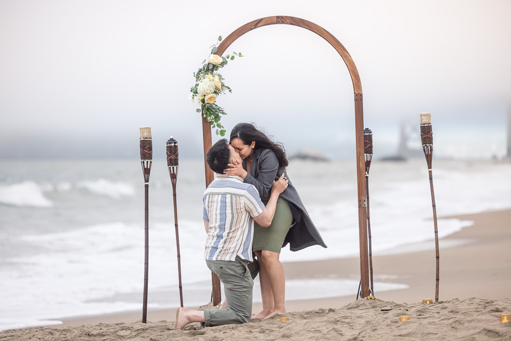 proposal at Baker Beach with wooden arch and torches on the sandy beach