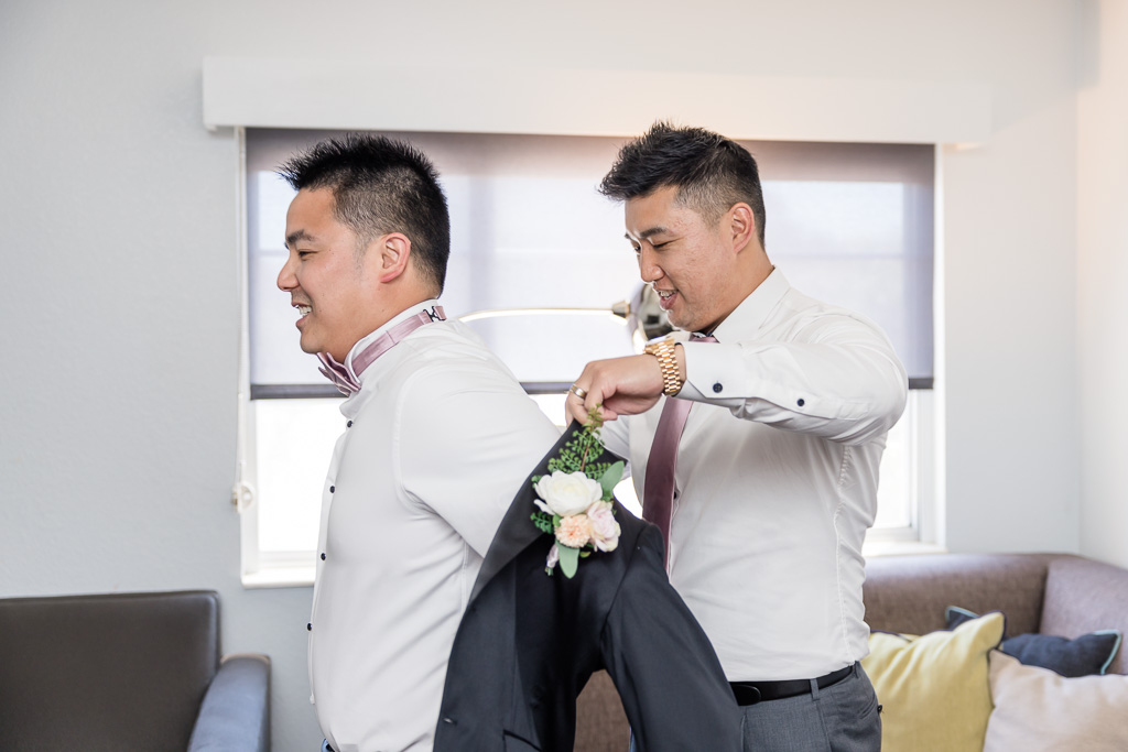 groom putting on suit jacket with help from his groomsman