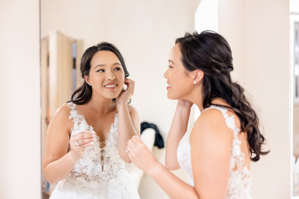 bride putting on earrings in front of mirror