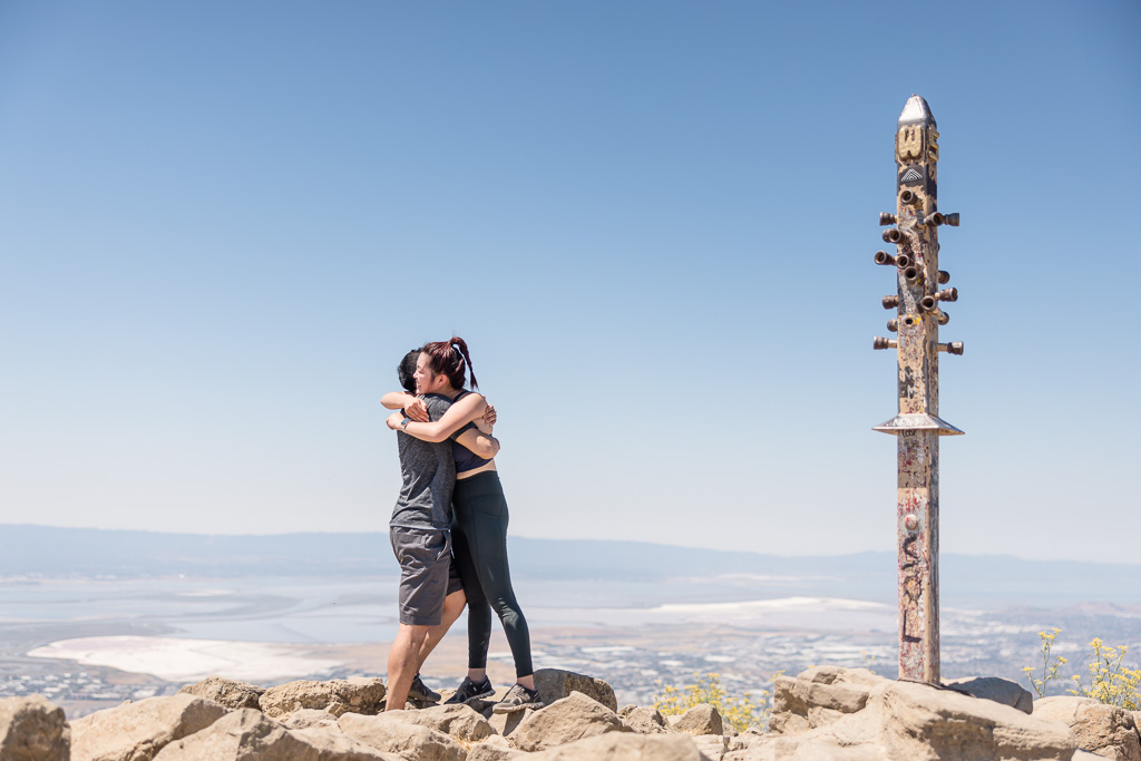 couple hugging at mountain peak marker pole