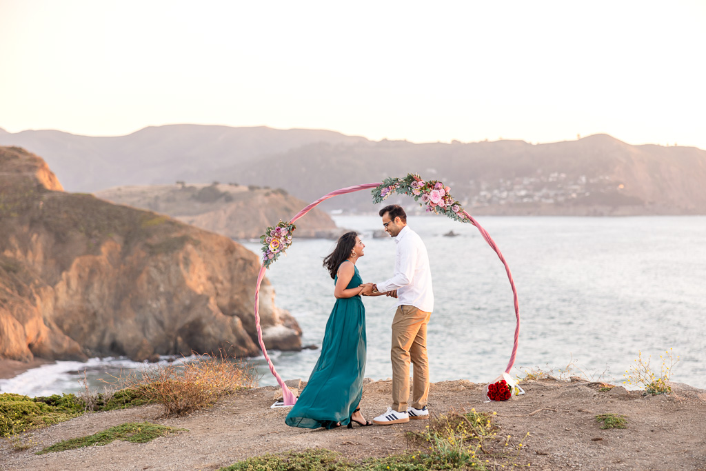 couple standing in front of a floral circular arbor on a cliffside