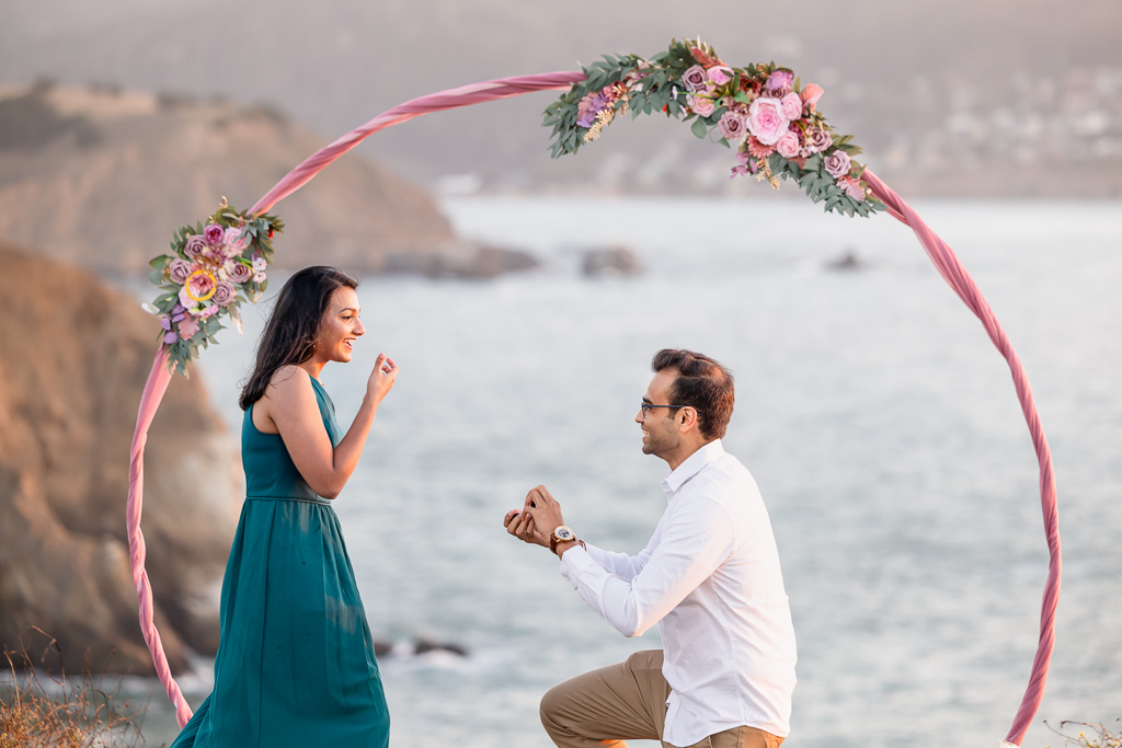 oceanside surprise proposal in front of floral arch