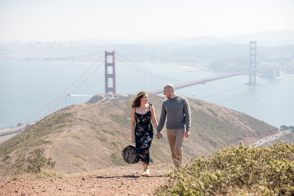 engagement photos of couple walking up hill with the Golden Gate Bridge behind them