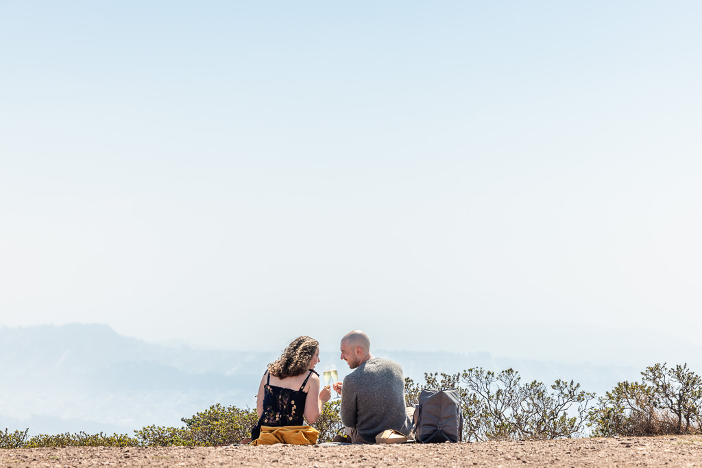 couple celebrating their engagement with champagne on a mountain overlooking city