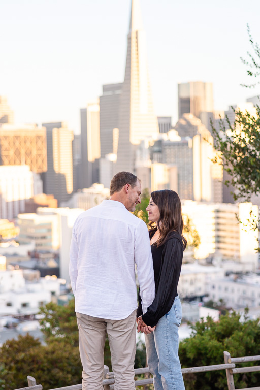 couple standing in an SF park with downtown behind them