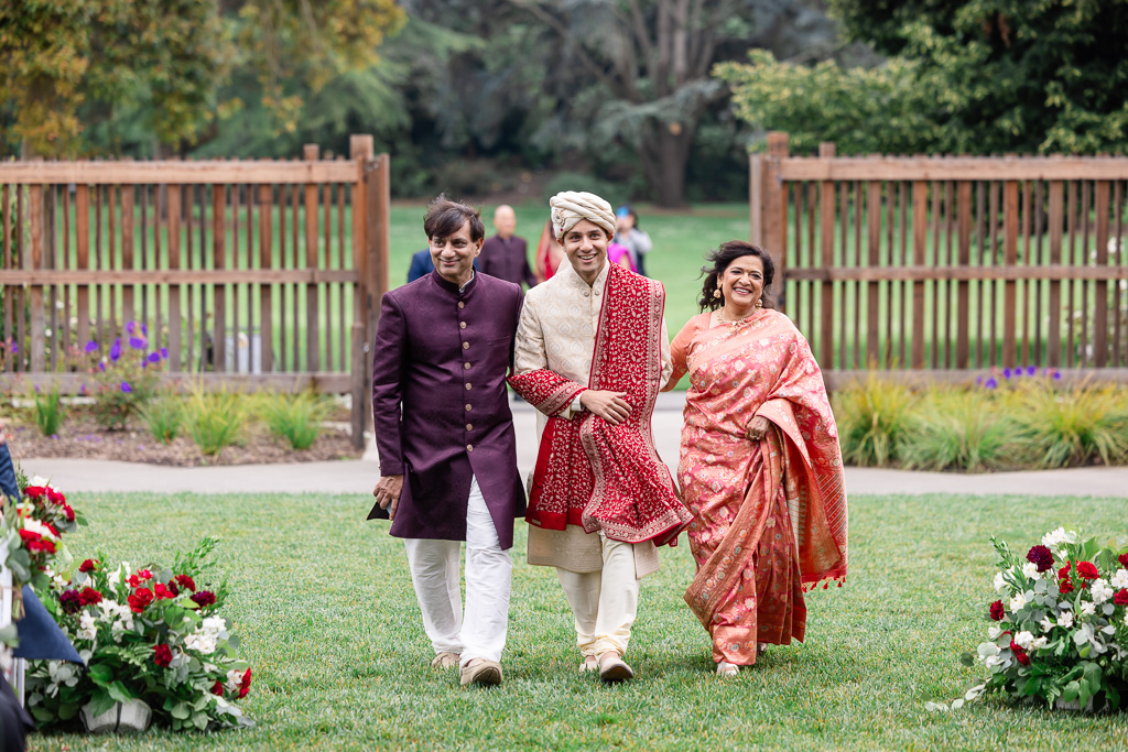 Indian groom walking down the aisle with both parents