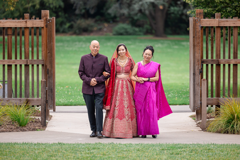 Asina bride dressed in Hindu attire walking down wedding aisle with both parents
