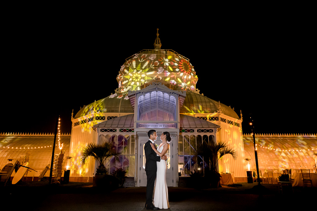 outdoor night wedding photo with lit-up Conservatory of Flowers behind couple