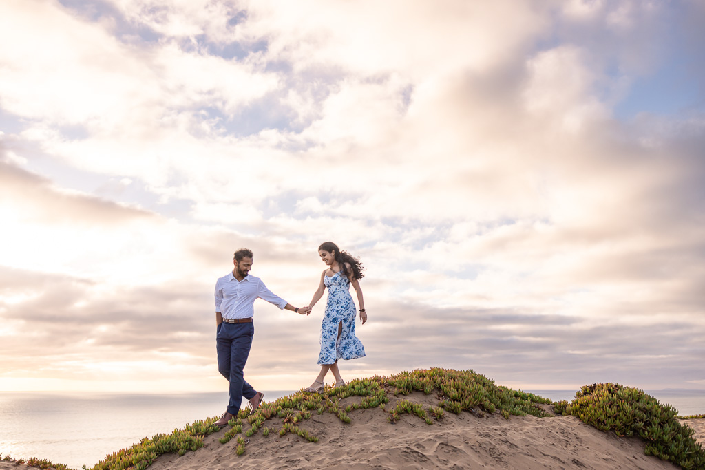 engagement photo of couple walking over a sand dune