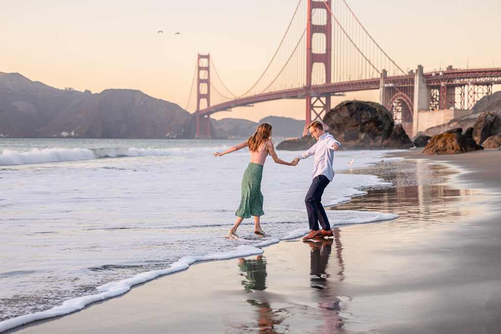 fun candid photo of couple splashing on the beach in front of the Golden Gate Bridge