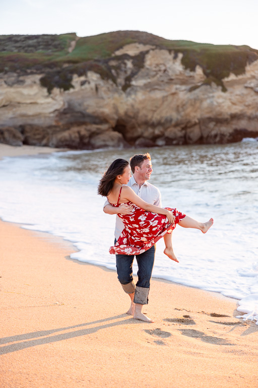 man carrying woman on tho beach for engagement photos