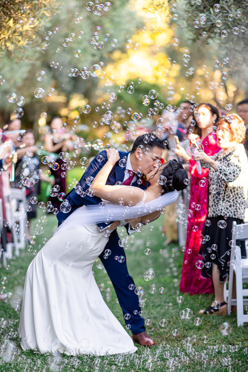bride and groom kissing as they walk back down the aisle with bubbles being blown by guests