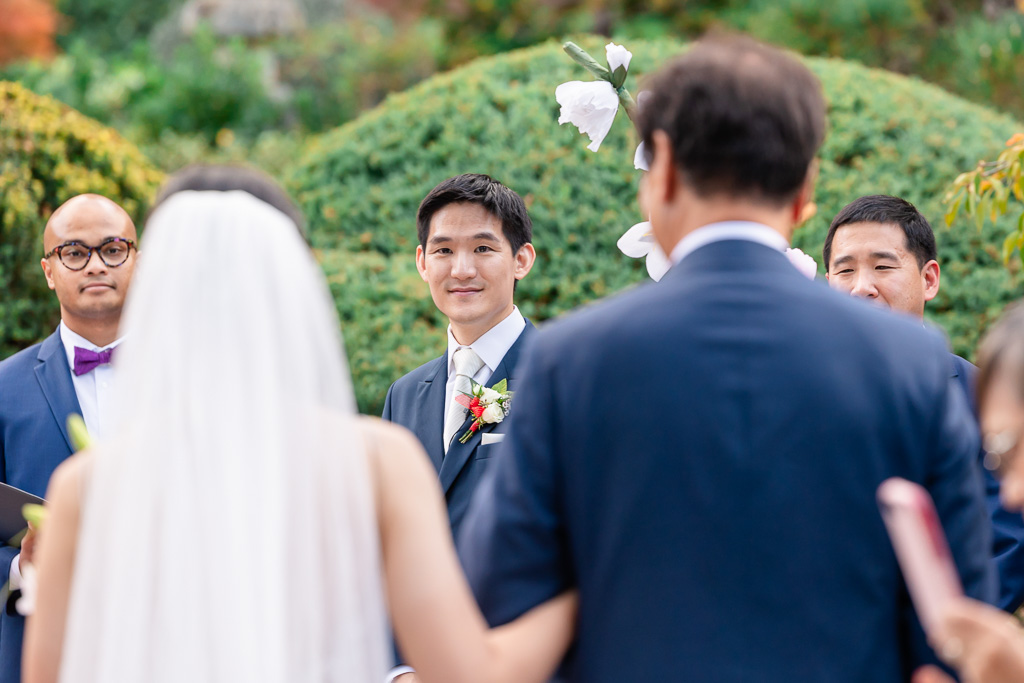 groom looking at bride as she walks down the aisle with her dad