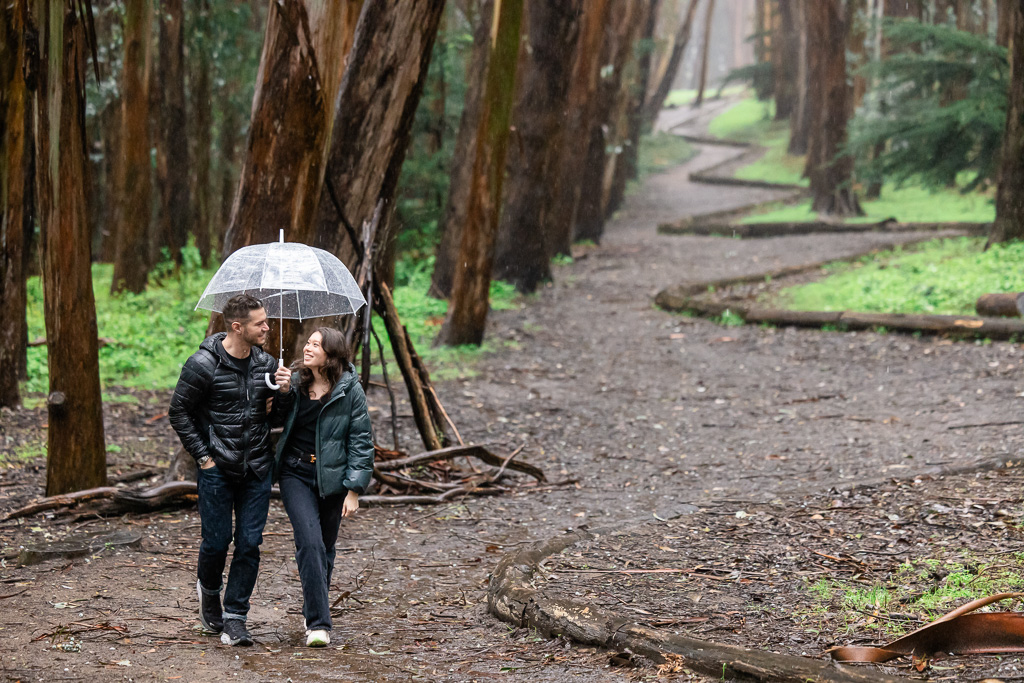 couple taking a walk in the woods on a rainy day with a clear umbrella at Lovers’ Lane