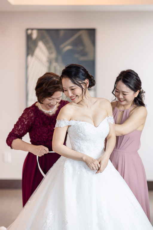 mom and bridesmaid helping bride with dress